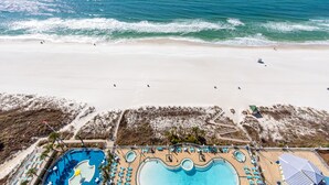 Vue aérienne d’un complexe hôtelier en bord de mer, avec une piscine, une plage et l’océan.