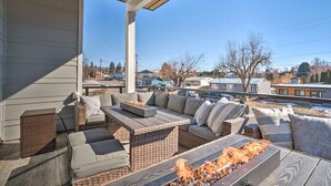 A covered outdoor seating area with a fire feature, wicker furniture, and a view of a residential neighborhood.
