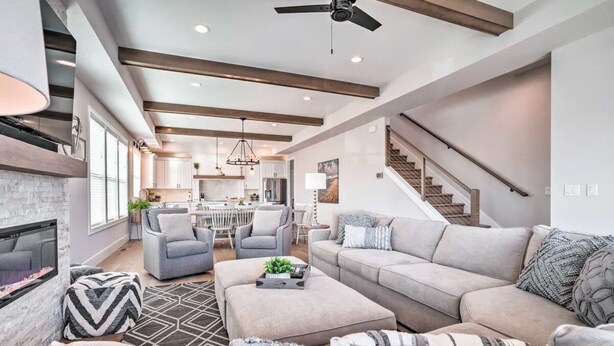 A modern living room with a fireplace, a sofa set, a dining area, and a staircase.