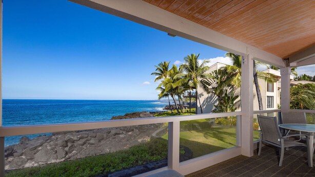 A covered outdoor seating area with a view of the ocean and palm trees.