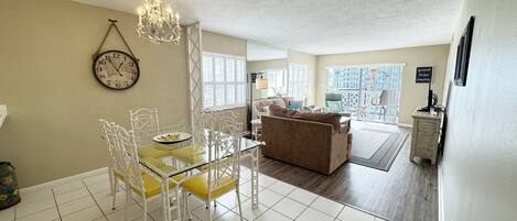 A dining area with a glass table and chairs, a chandelier, and a clock on the wall.