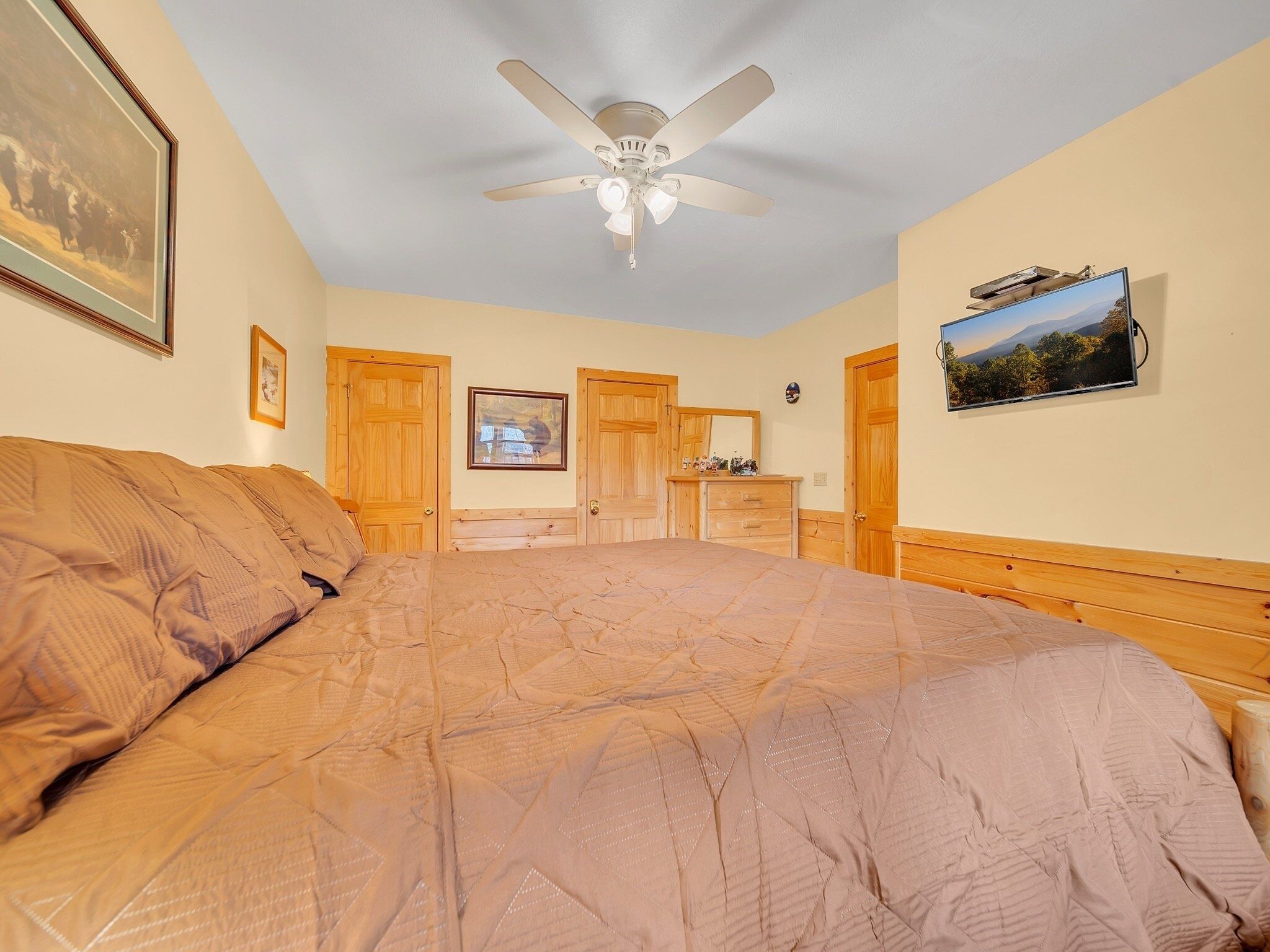 A bedroom with a bed, a ceiling fan, wooden doors, a dresser, and a framed picture on the wall.