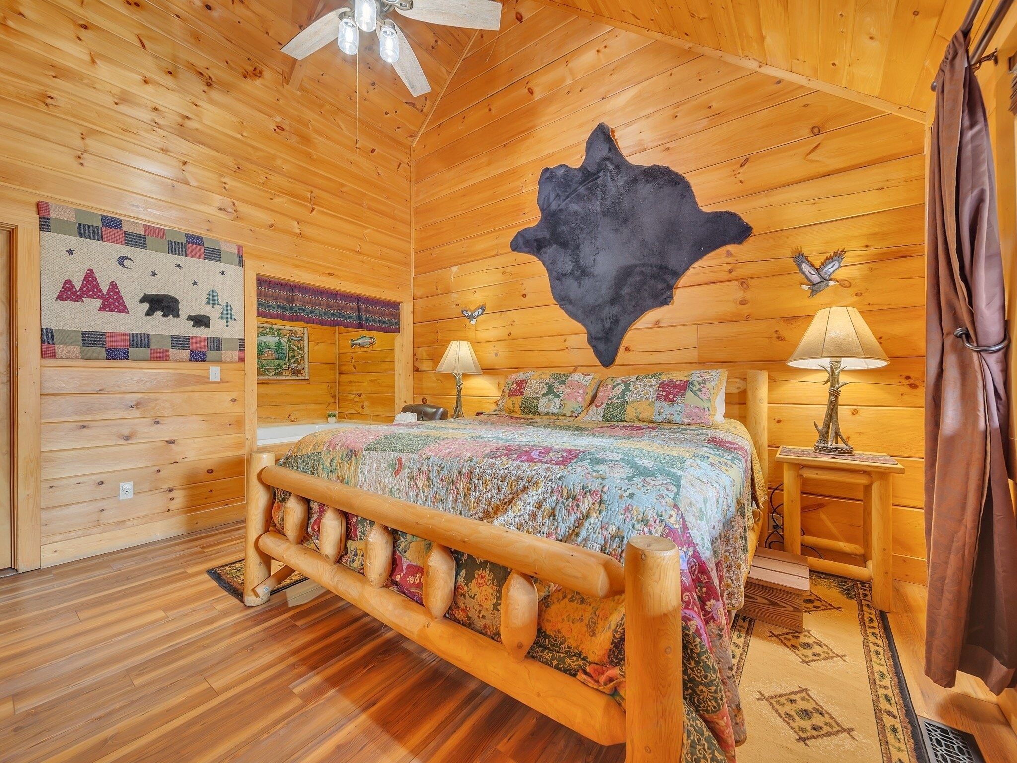 A wooden cabin bedroom with a bed, two nightstands, a ceiling fan, and a wall-mounted animal hide.