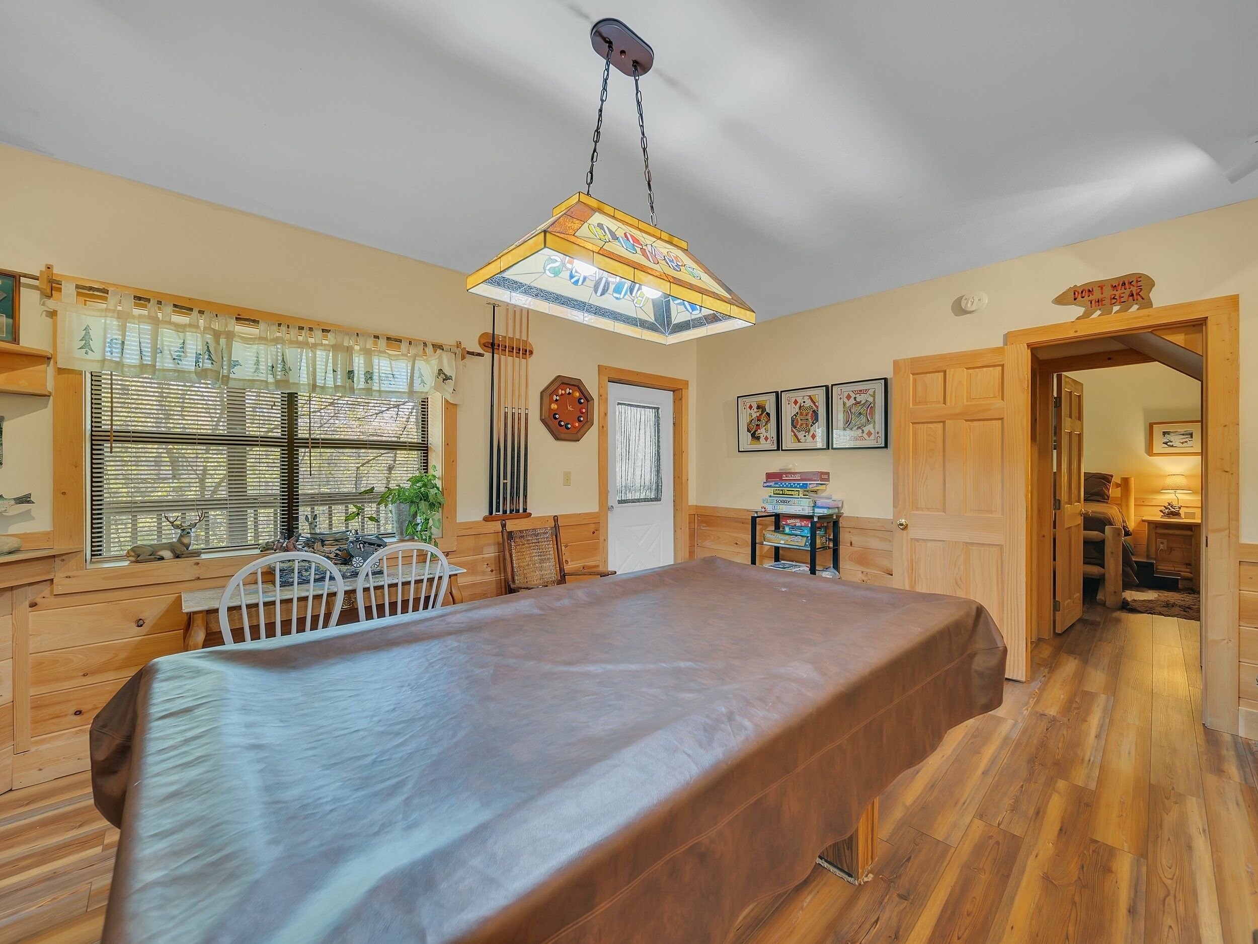A cozy room with a wooden dining table, a chandelier, and a window with blinds.