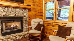 A cozy cabin interior with a stone fireplace, wooden walls, and two upholstered chairs. - Er97 - Squirrel's Retreat - Close To The Action In Pigeon Forge! 2 Bedroom Cabin by RedAwning (Pigeon Forge)