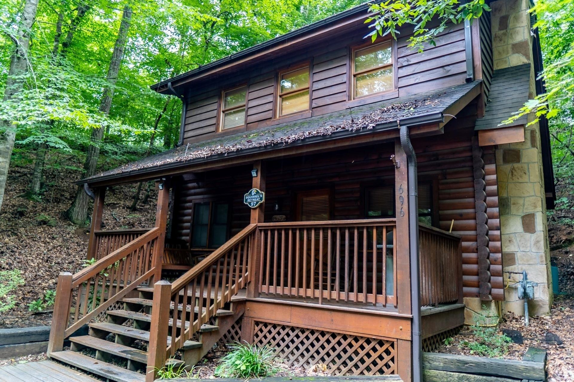 A rustic cabin with a wooden staircase leading to a porch, surrounded by trees.