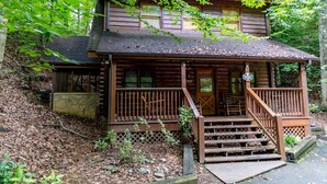 A two-story log cabin with a porch, stone foundation, and a sign indicating it is a campground. - Er97 - Squirrel's Retreat - Close To The Action In Pigeon Forge! 2 Bedroom Cabin by RedAwning (Pigeon Forge)