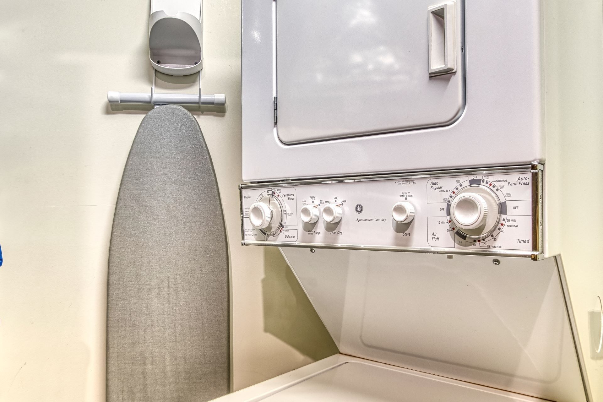 A front-loading washing machine with control knobs and a drying rack.