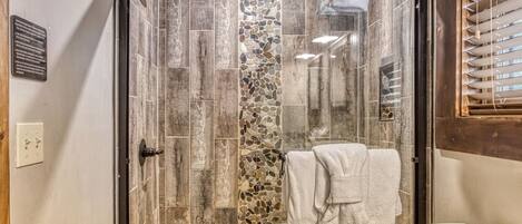 A glass-enclosed shower with a stone mosaic wall, a towel hanging on the door, and a wooden-framed window.