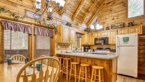 A wooden cabin kitchen with a central island, bar stools, and a refrigerator. - Er308- The Cozy Bear- Great Location- Close To Town 2 Bedroom Cabin by RedAwning (Pigeon Forge)