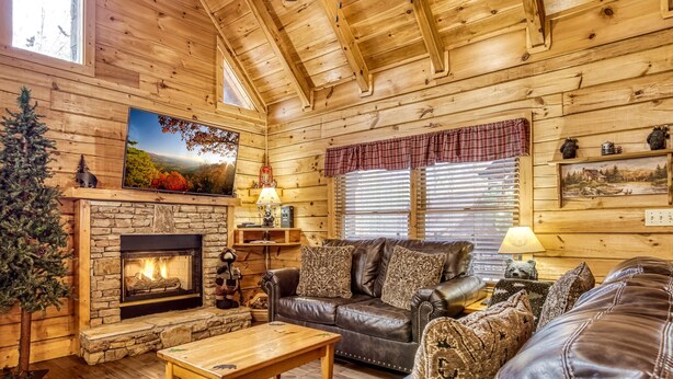 A cozy log cabin interior with a stone fireplace, leather furniture, and a large window with blinds. - Er308- The Cozy Bear- Great Location- Close To Town 2 Bedroom Cabin by RedAwning (Pigeon Forge)
