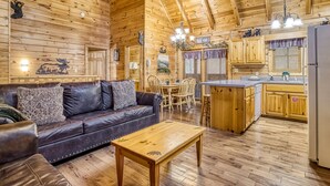 A cozy cabin interior with a wooden ceiling, a leather sofa, a dining table, and a kitchen area. - Er308- The Cozy Bear- Great Location- Close To Town 2 Bedroom Cabin by RedAwning (Pigeon Forge)