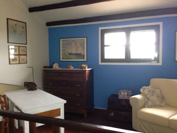 A room with a blue wall, a wooden dresser, a white table, and a beige armchair.