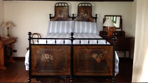 Una cama de madera tradicional con estructura metálica, una mesita de noche con lámpara, y un espejo en la pared.