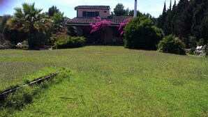 Una casa con tejado de baldosas, rodeada por un campo cubierto de hierba y varios árboles.