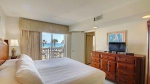 Habitación de hotel con una cama grande, un aparador de madera, un televisor y un balcón con vista al océano.