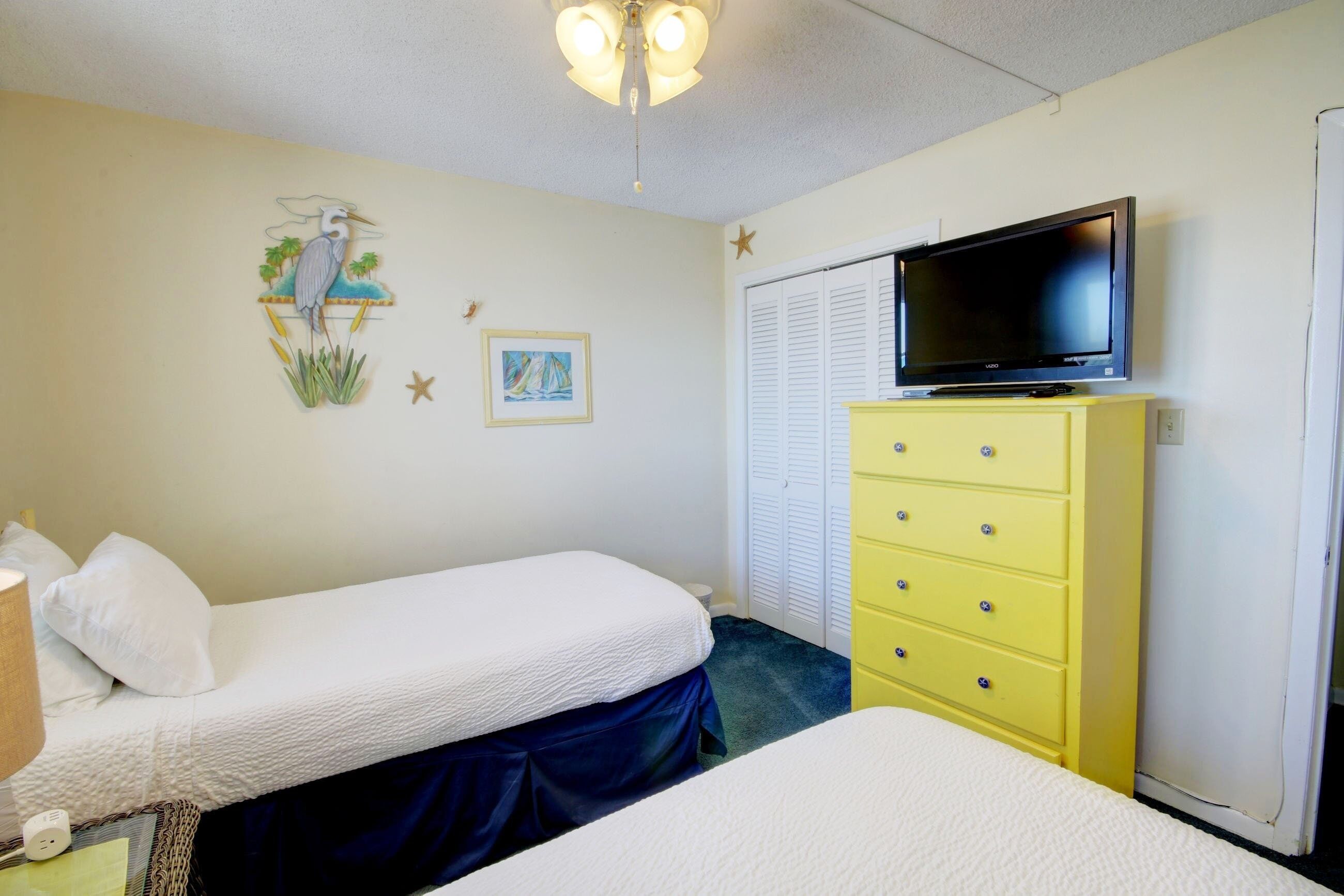 A bedroom with two beds, a television on a dresser, and a ceiling fan.