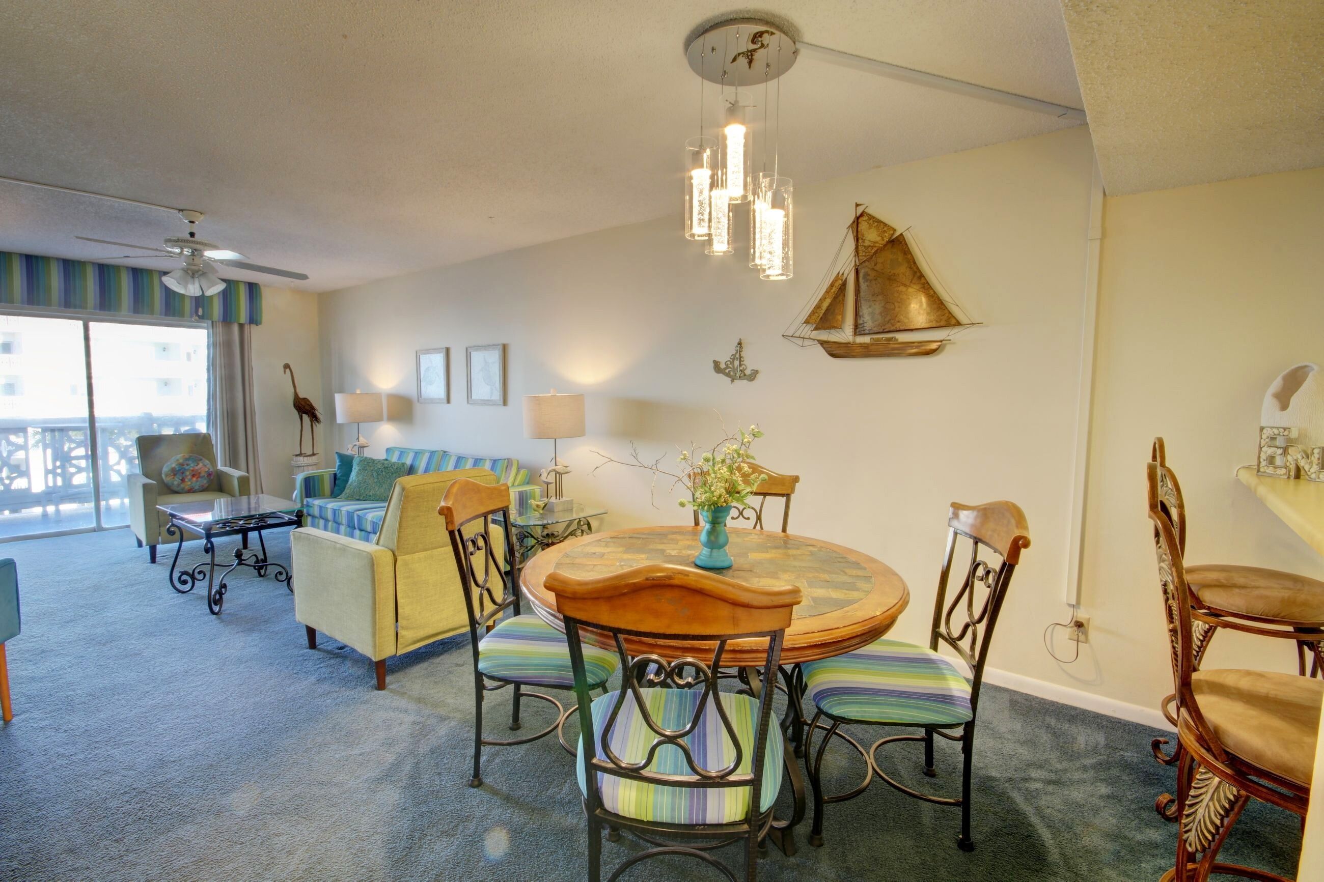 A dining area with a round table, chairs, and a chandelier. There is a sofa and a chair in the background.