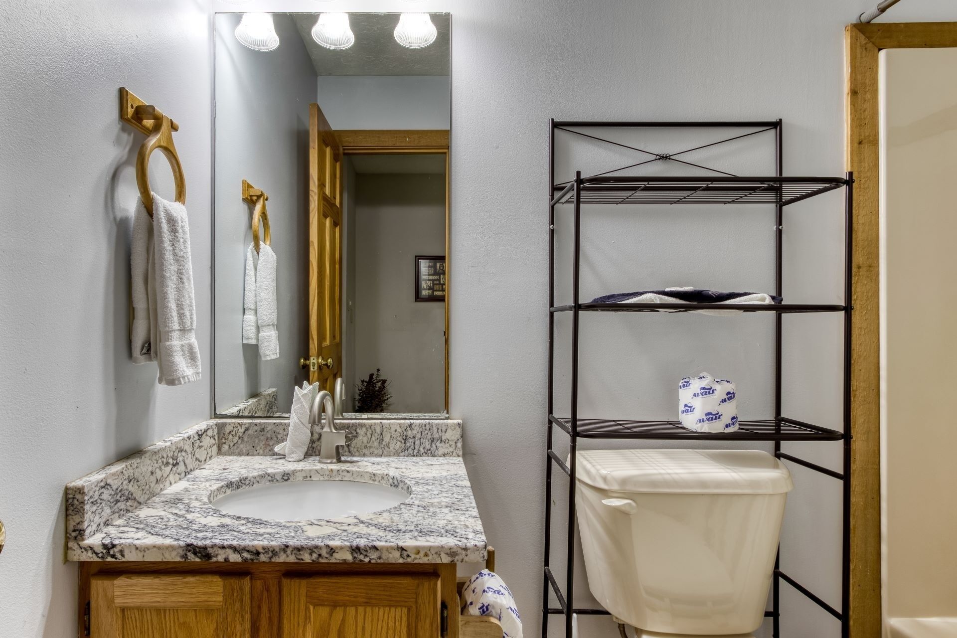 A bathroom with a marble sink, wooden vanity, a towel rack, a mirror, and a black metal shelf with a toilet.