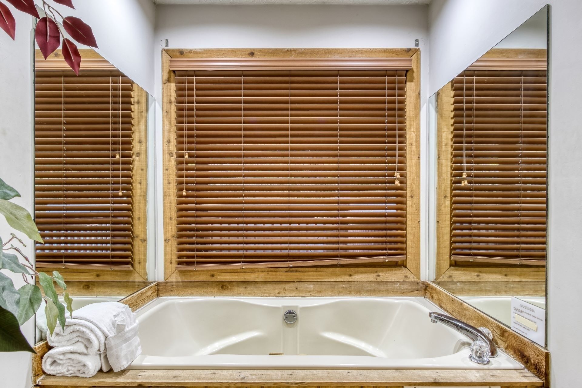 Un baño con ventana de madera, una bañera blanca y un lavamanos con grifo.
