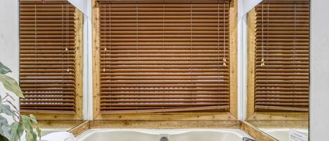 Un baño con ventana de madera, una bañera blanca y un lavamanos con grifo.