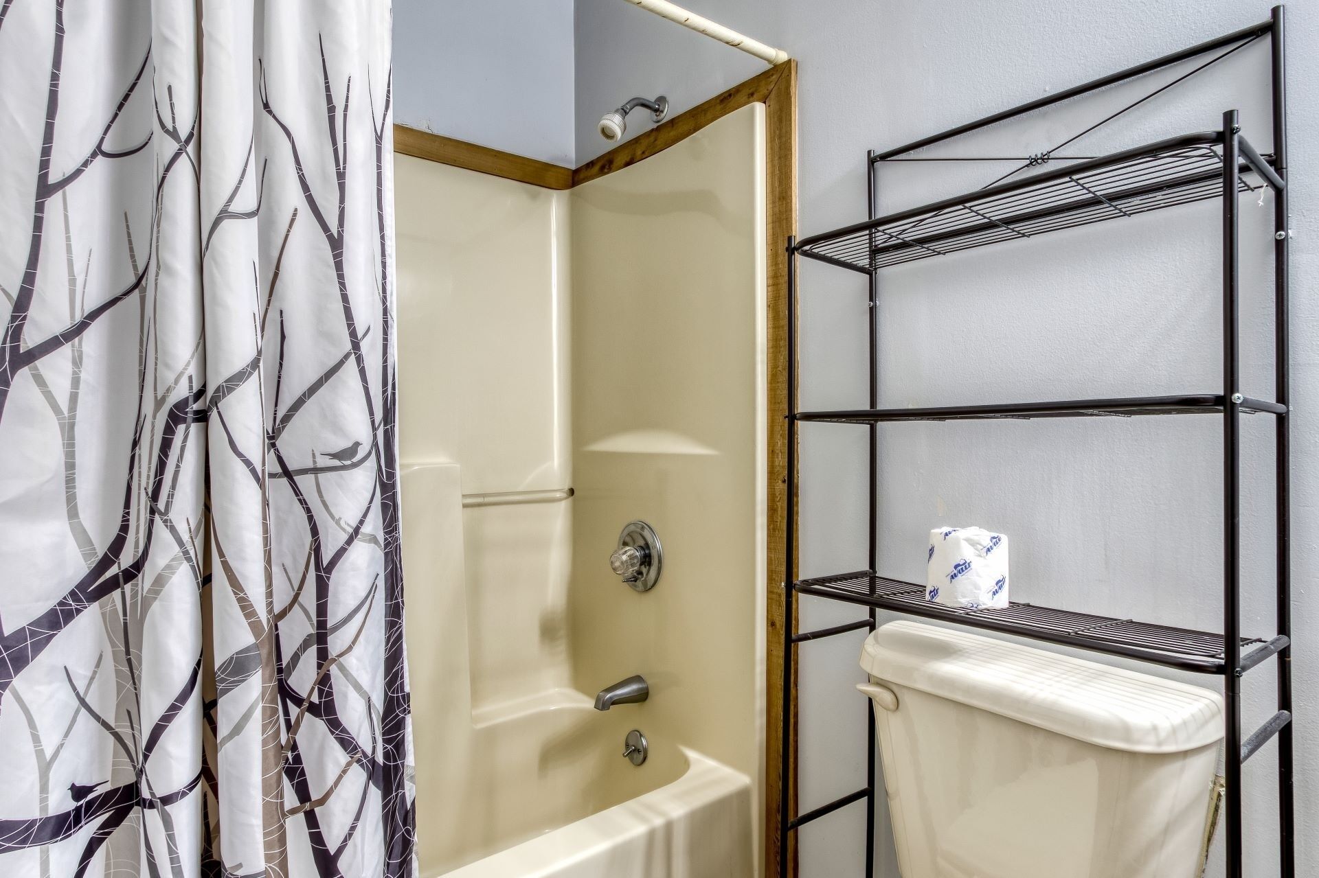 A bathroom with a bathtub, a shower, and a toilet. There is a metal shelf unit with a toilet paper roll on it.