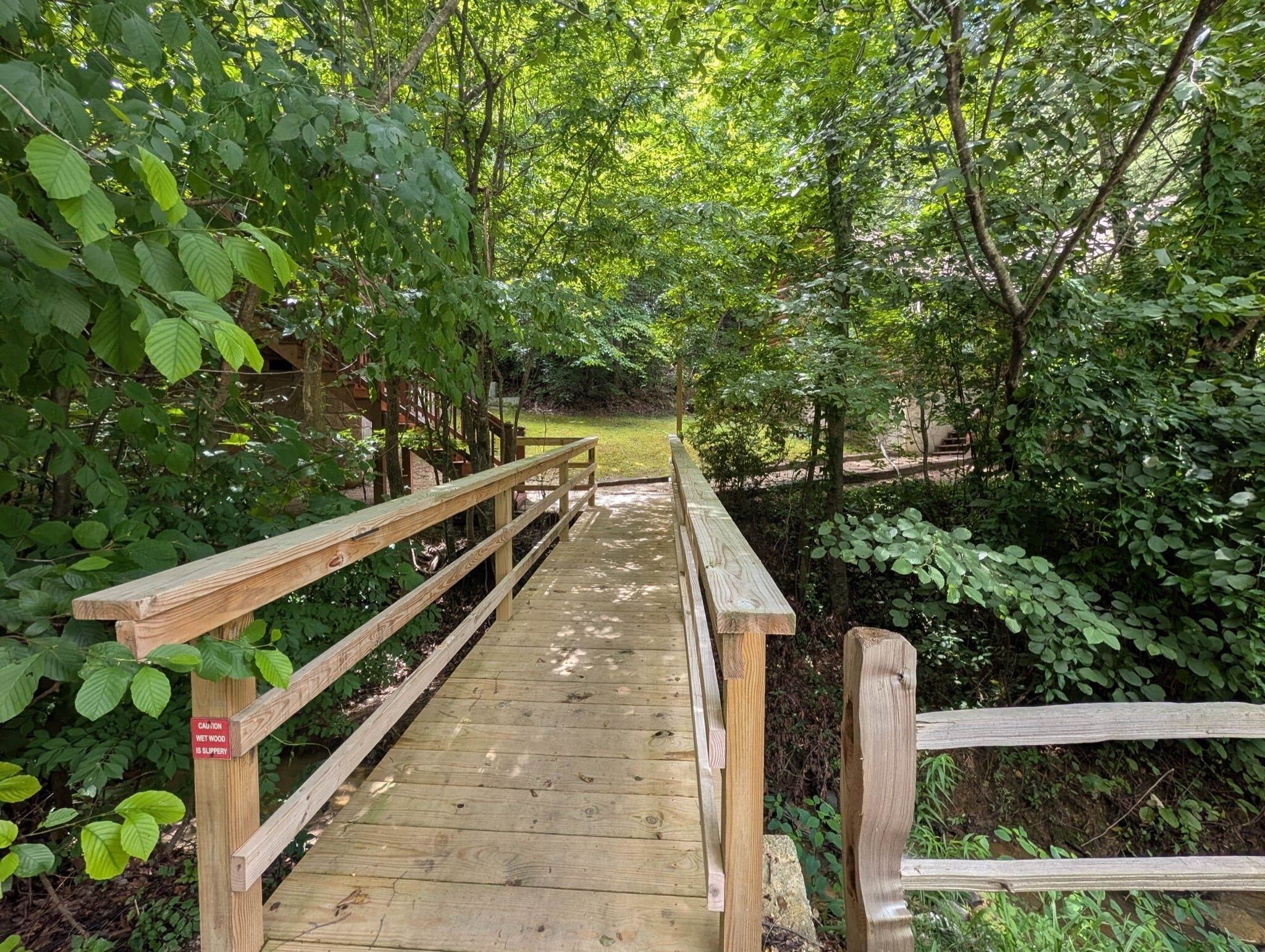 Un pont en bois sur lequel est affiché un panneau d’avertissement indiquant que le bois est glissant lorsqu’il est mouillé.