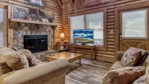 A cozy log cabin interior with a stone fireplace, a television, and rustic wooden furniture. - Er33 Ganma's Getaway Great Location, close To Town 4 Bedroom Cabin by RedAwning (Pigeon Forge)