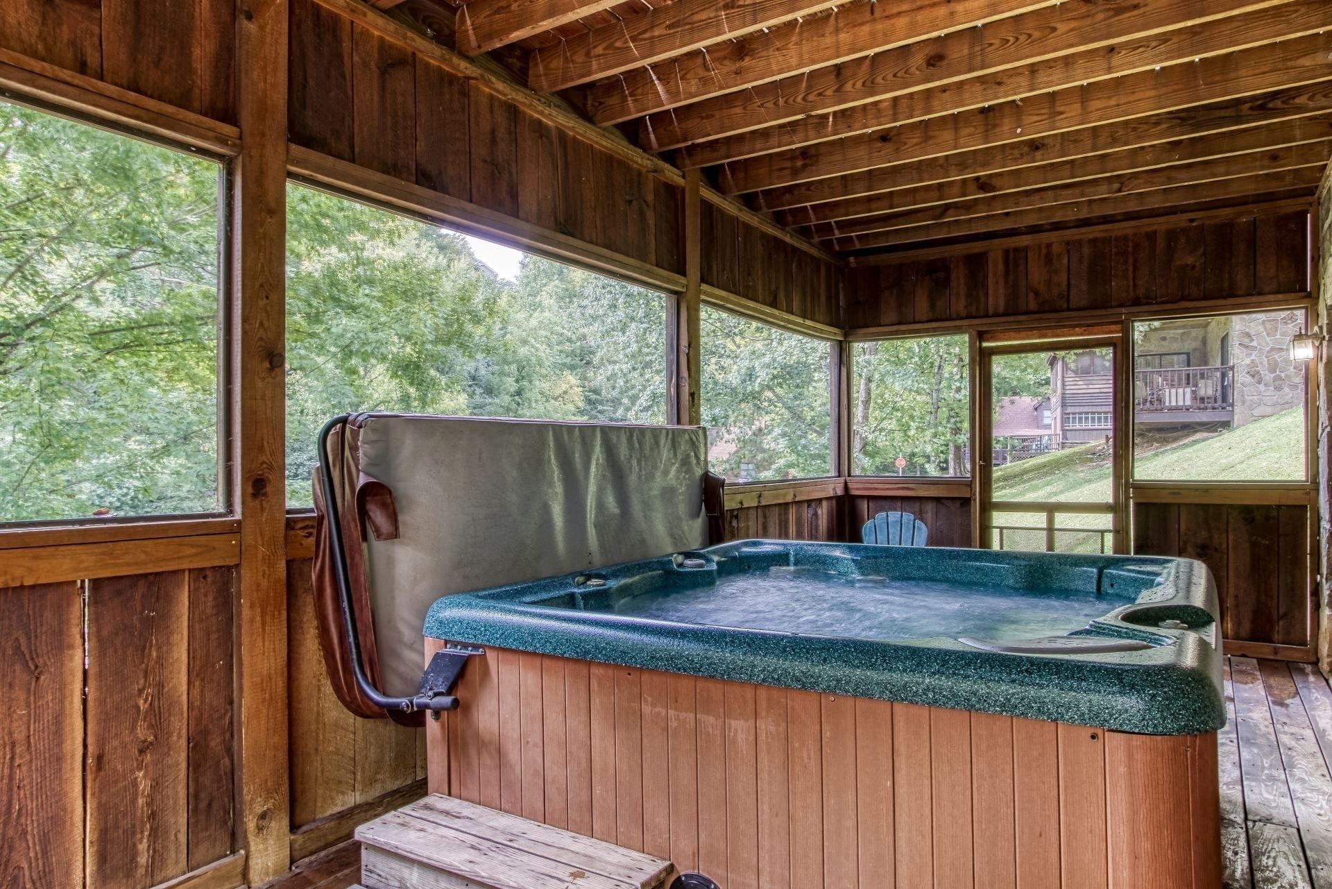 A wooden cabin with a hot tub, large windows, and a view of the surrounding forest.