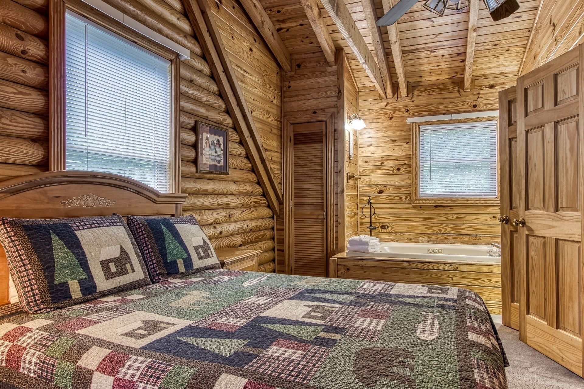 A log cabin bedroom with a wooden bed, a large window, a door, and a bathtub.