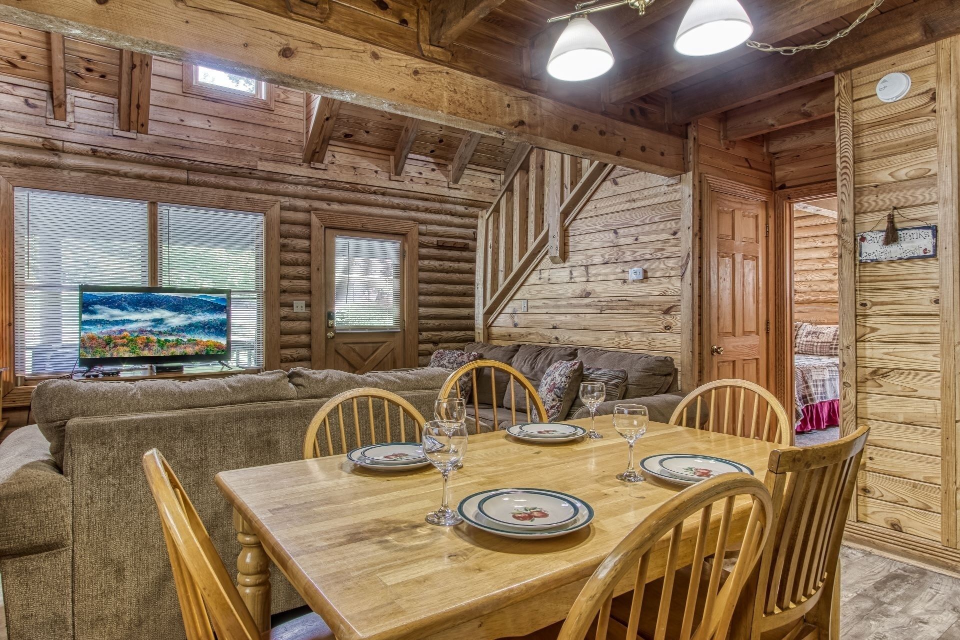 A cozy log cabin interior with a dining area, a sofa, and a TV displaying a scenic landscape.
