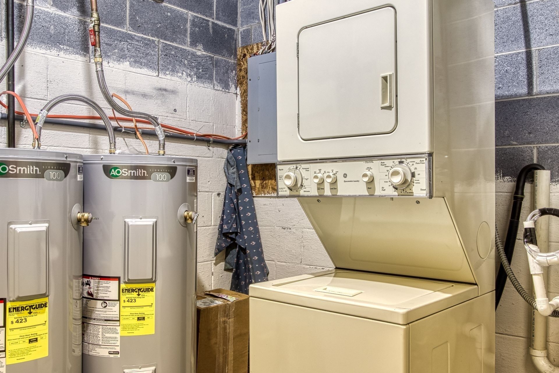 A utility room with two AOSmith water heaters, a washing machine, and various pipes and controls.