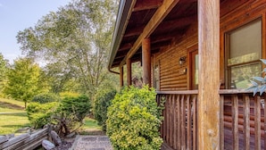 A rustic log cabin with a wooden porch, a small garden area with shrubs, and a gravel pathway leading to the entrance. - Er33 Ganma's Getaway Great Location, close To Town 4 Bedroom Cabin by RedAwning (Pigeon Forge)