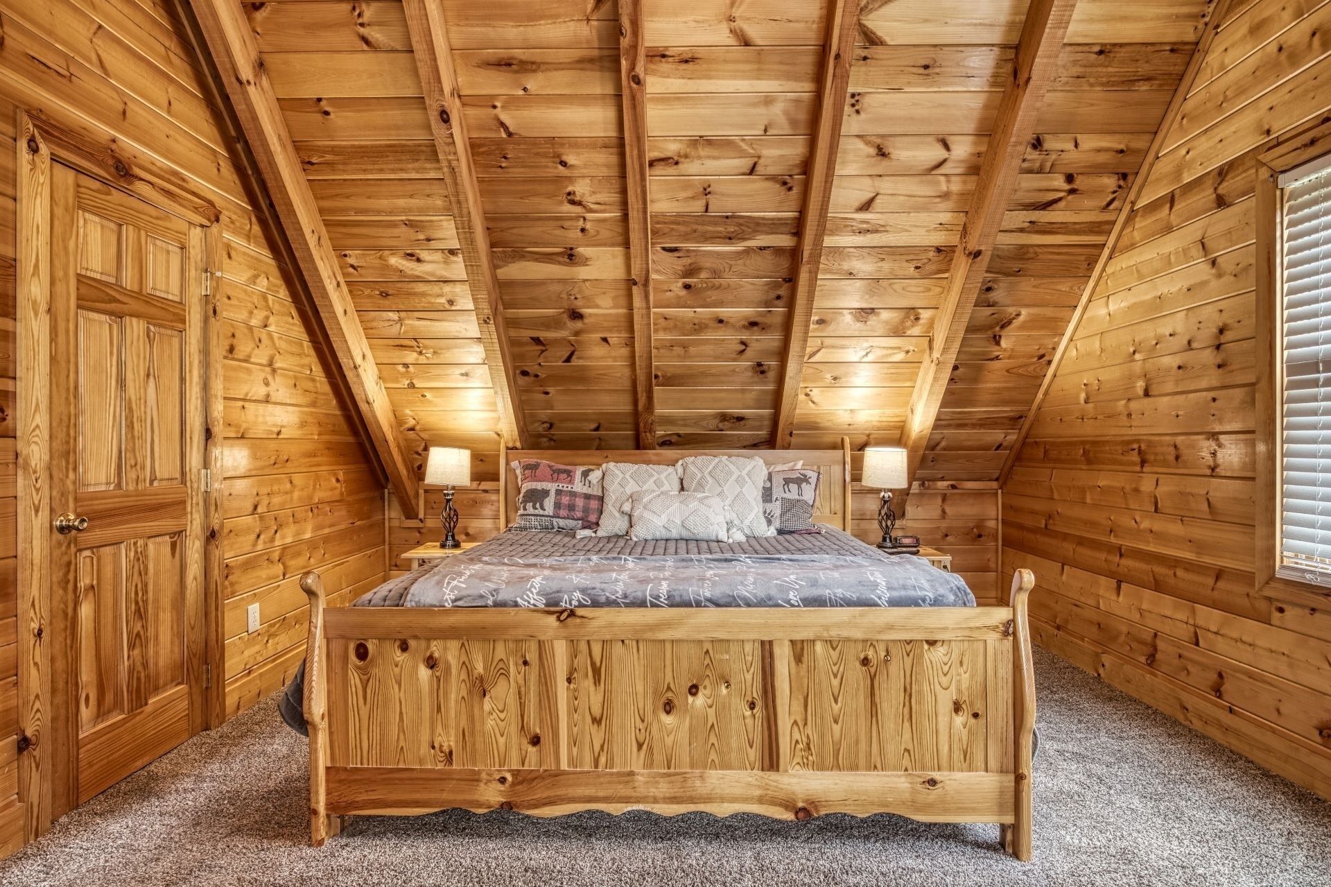 Ein gemütliches Schlafzimmer im Dachgeschoss mit einem hölzernen Bett, zwei Nachttischlampen und einem Fenster mit Jalousien.