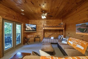 L’intérieur d’un chalet en bois est aménagé avec un téléviseur, des lits superposés, un canapé et une table à manger.