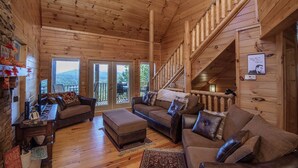 A cozy log cabin interior with a living room, a staircase, and a view of the outdoors. - Dunder Mountain Views Cabin Retreat 3 Bedroom Cabin by RedAwning (Sevierville)