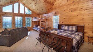 A cabin with a loft bed, a sofa, a dining table, and multiple windows offering views of the forest. - Dunder Mountain Views Cabin Retreat 3 Bedroom Cabin by RedAwning (Sevierville)