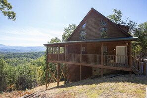 Une cabane en bois dotée d’un balcon, située dans une zone boisée et offrant une vue sur les montagnes lointaines.