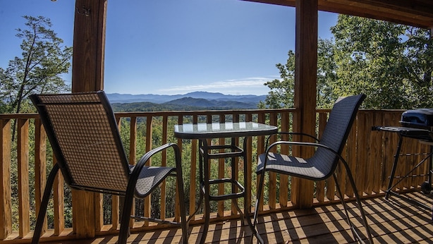 A wooden deck with two wicker chairs and a glass table, overlooking a mountainous landscape. - Dunder Mountain Views Cabin Retreat 3 Bedroom Cabin by RedAwning (Sevierville)
