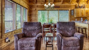 A cozy cabin interior with two plush armchairs, a wooden dining table, and a chandelier. - Ern857 - A Dream Come True - Great Location! Close To All The Action! 3 Bedroom Cabin by RedAwning (Pigeon Forge)