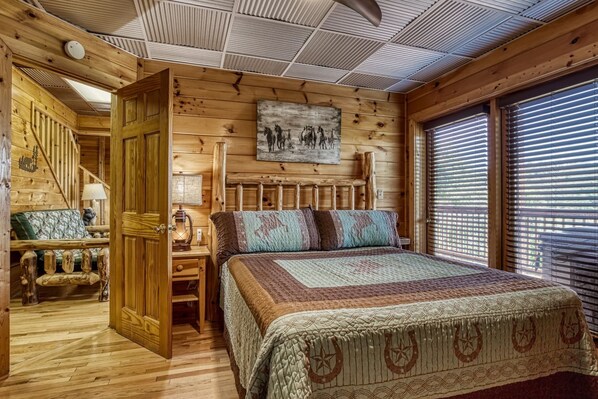 Un dormitorio de cabaña de troncos con una cama, una mesita de noche, una lámpara, un cuadro y una ventana con persianas.
