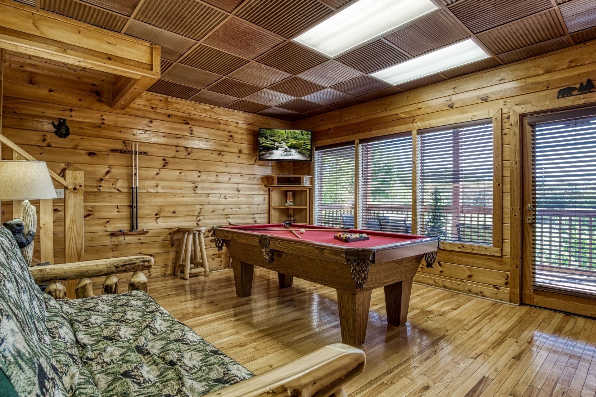 A wooden interior with a pool table, a sofa, and a lamp.