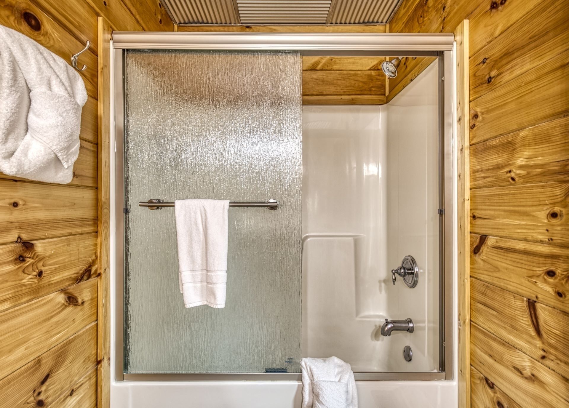 A bathroom with a glass-enclosed shower, wooden walls, a towel rack, and a bathtub.