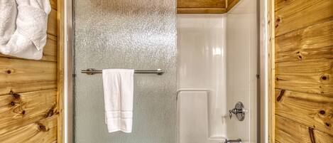 A bathroom with a glass-enclosed shower, wooden walls, a towel rack, and a bathtub.