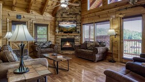 A cozy cabin interior with wooden walls, a stone fireplace, leather sofas, and a ceiling fan. - Ern857 - A Dream Come True - Great Location! Close To All The Action! 3 Bedroom Cabin by RedAwning (Pigeon Forge)