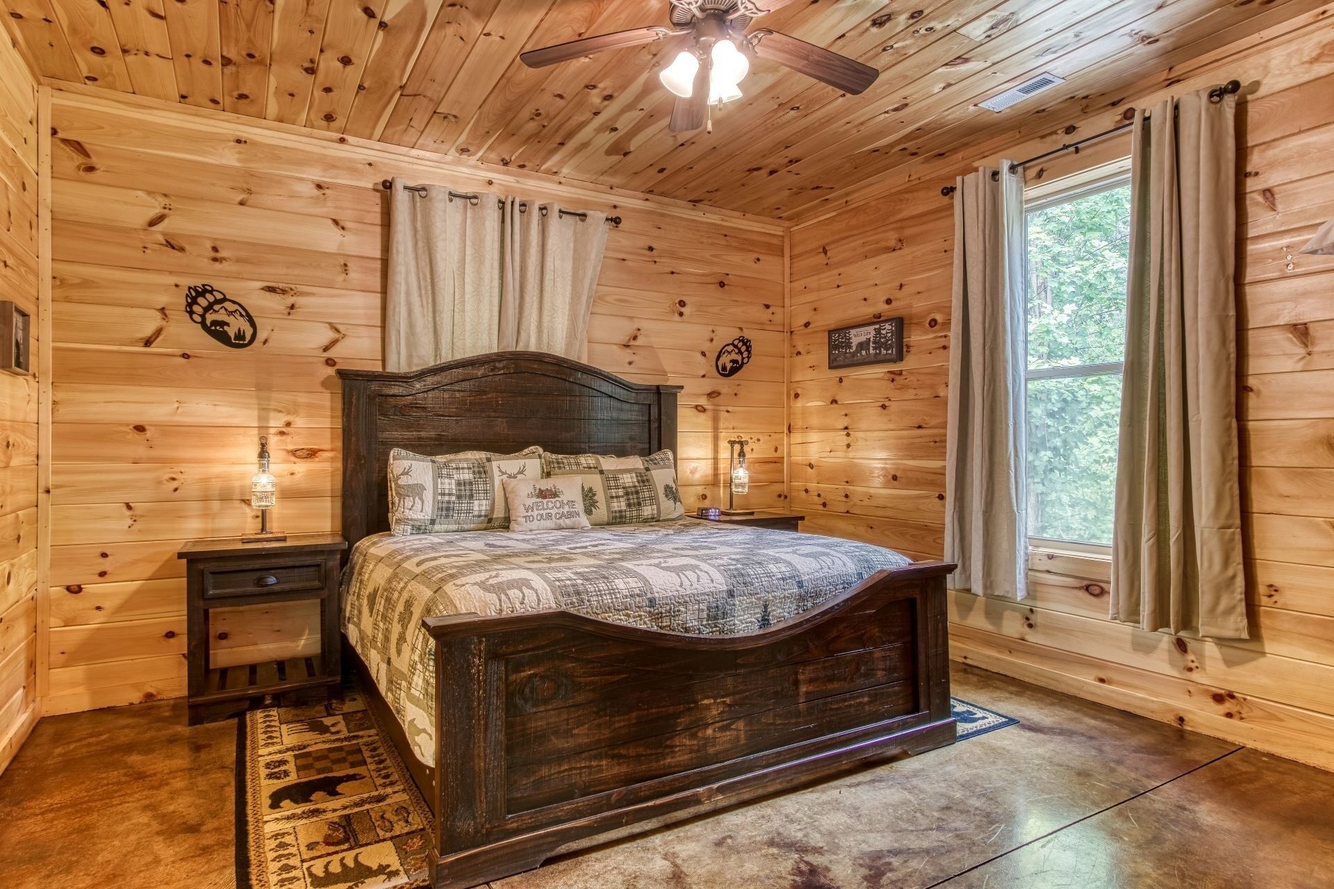 Camera da letto in una baita di legno, con un letto, comodini, una ventola a soffitto e una finestra con tende.