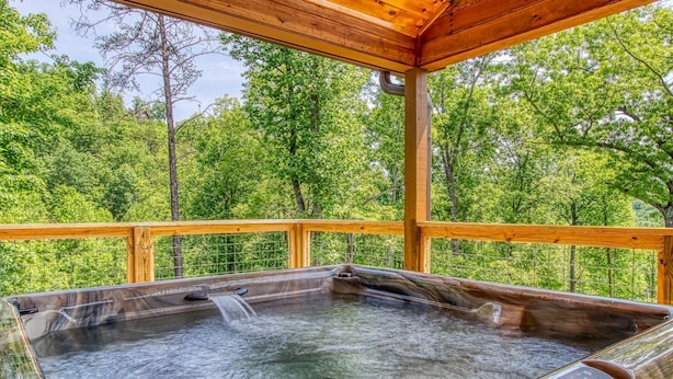 Ein Whirlpool mit einer Holzterrasse und Blick auf einen Wald.
