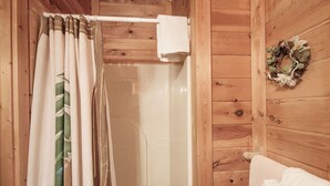 A wooden cabin bathroom with a shower, a towel rack, and a wreath on the wall. - Er36 - Cozy Creekside Great Location- Close To Town 1 Bedroom Cabin by RedAwning (Pigeon Forge)