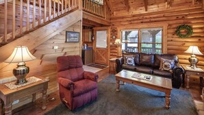 A cozy log cabin interior with a staircase, a leather sofa, a red armchair, and a wooden coffee table. - Er36 - Cozy Creekside Great Location- Close To Town 1 Bedroom Cabin by RedAwning (Pigeon Forge)