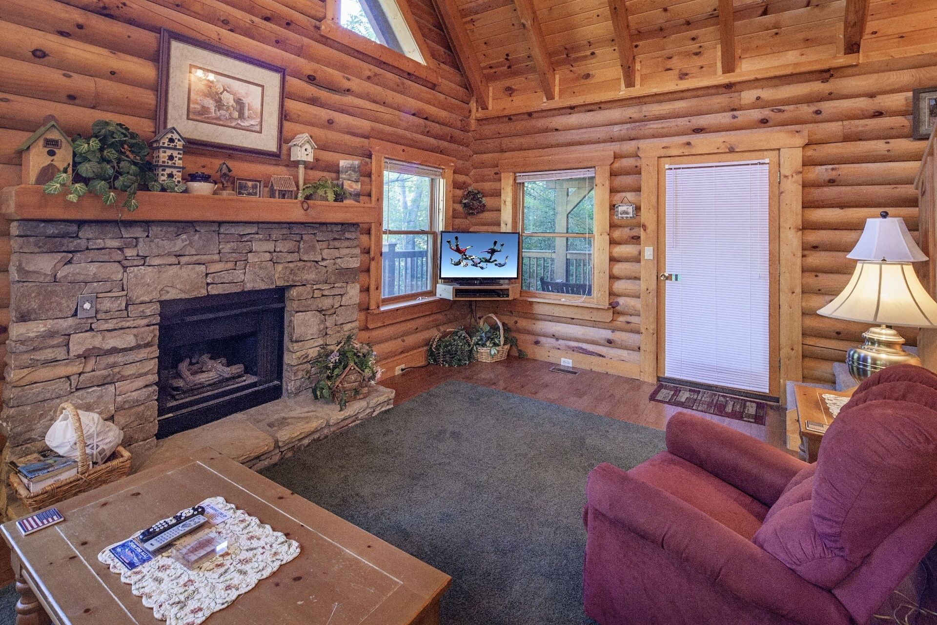 A cozy log cabin interior with a stone fireplace, a television, and a comfortable seating area.